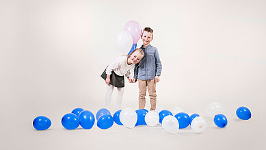Ein Mädchen und ein Junge freuen sich über viele Luftballons.